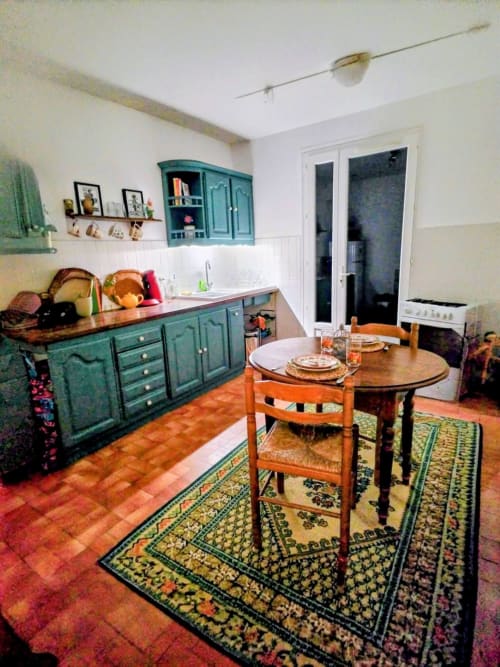 Charming kitchen and dining area in a dog-friendly French villa with turquoise cabinetry, wooden table, and traditional tile