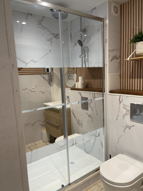Salle de bain moderne avec douche vitrée, carrelage imitation marbre et meuble vasque en bois à l'appartement La Montagnette, Cap d'Agde
