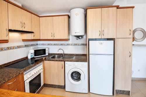 Cocina moderna en Apartamentos El Calón Playa con muebles de madera, encimeras de granito y electrodomésticos incluyendo lavadora
