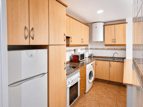 Modern kitchen in Apartamentos El Calón Playa with wooden cabinets, granite countertops, stove, washing machine, and full
