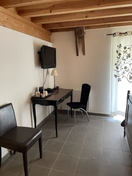 Coin séjour du gîte Les Pratges à Figeac avec bureau noir, chaise, télévision et poutres en bois