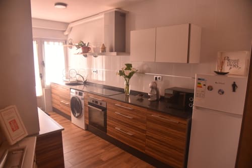 Modern kitchen in Benavente apartment with wood cabinets, black countertop, washing machine, and white upper cabinets
