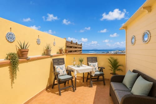 Terrasse ensoleillée sur le toit de l'hôtel Sara & Gino à Corralejo avec vue mer, table à manger, sièges confortables et plantes en pot