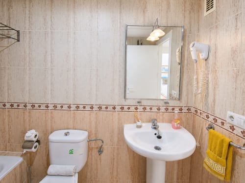 Bathroom in Apartamentos El Calón Playa with pedestal sink, toilet, mirror, and yellow towel in Cuevas del Almanzora