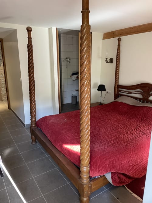 Lit à colonnes avec literie rouge dans une chambre de cottage aux Pratges, Figeac, avec salle de bain attenante visible