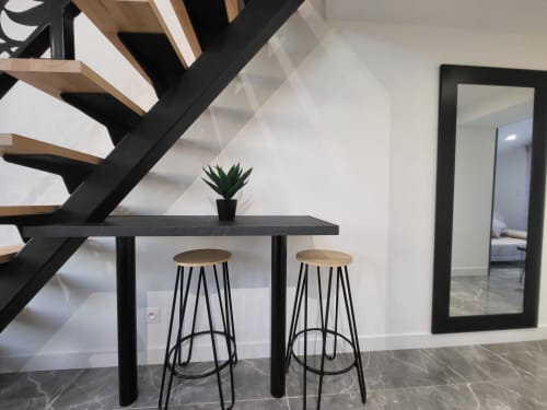 Escalier moderne aux marches noires et bois, table noire avec deux tabourets de bar, plante en pot et miroir mural aux Gites Les