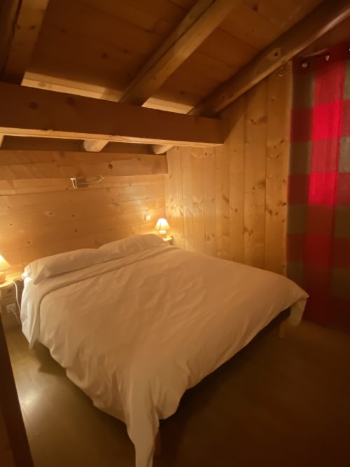 Chambre douillette à La Ferme des Georgières avec literie blanche, poutres apparentes, éclairage chaleureux et mur d'accent rouge