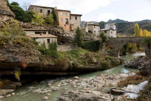 Edificios históricos de piedra en Montgat, ES, ubicados en las estribaciones de los Pirineos con vistas a un río y las montañas