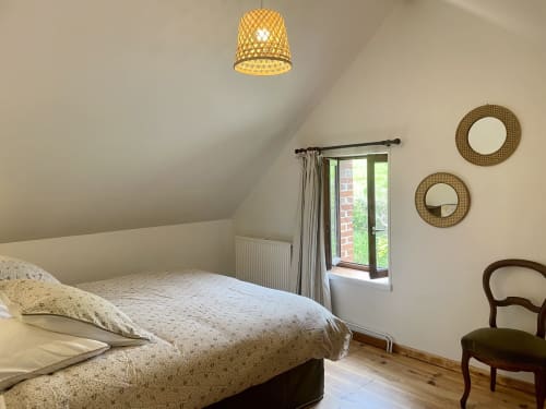 Chambre lumineuse sous les toits du Château de Vaux Morvan avec luminaire tressé, portes donnant sur le jardin et miroirs décoratifs