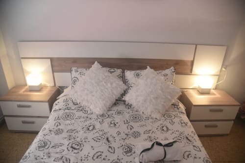 Benavente apartment bedroom with floral patterned bedding, white decorative pillows, wooden headboard, and bedside lamps.