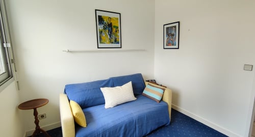 Coin salon cosy avec canapé bleu, coussins blancs et cadres d'art dans l'appartement Mer et Maisons, La Trinité sur Mer