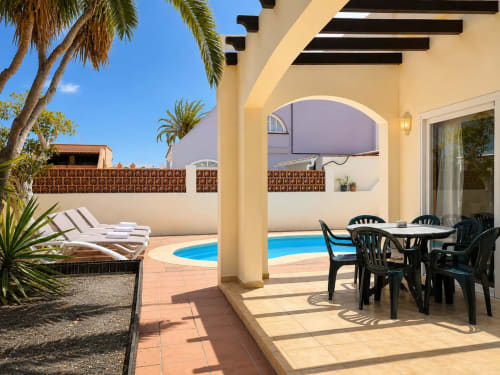 Terraza de piscina Villa Paloma con tumbonas, mesa de comedor y piscina azul en Corralejo, Fuerteventura