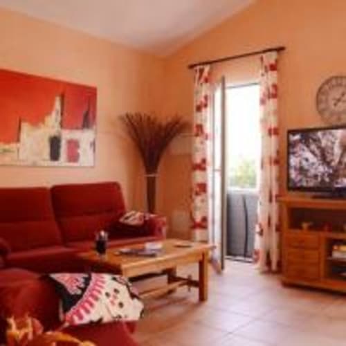 Luminoso salón naranja en villa Las Golondrinas con sofá rojo, muebles de madera y vistas a la piscina en Cap d'Artrutx
