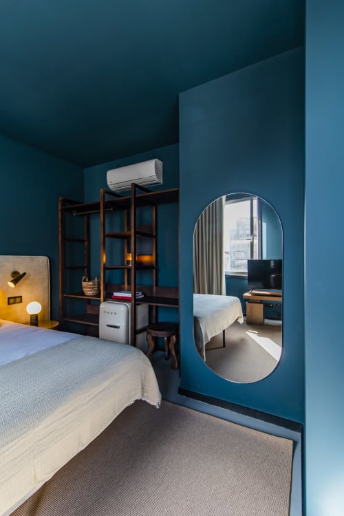 Modern bedroom at Benefit Collection hotel in Porto with teal walls, bed, wooden shelving, and oval mirror reflecting the