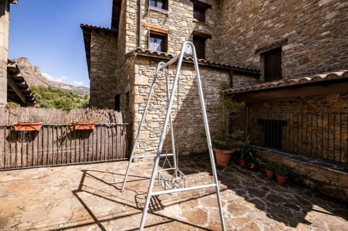 Columpio en patio de complejo residencial de piedra en Montgat Prepirénées con vistas a montañas y arquitectura tradicional