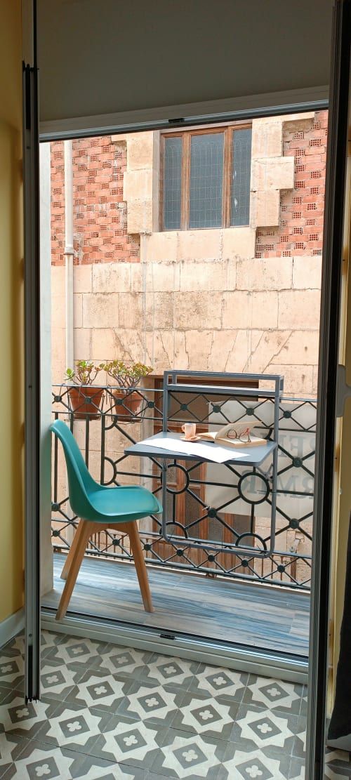Silla turquesa en escritorio en balcón soleado con vista a patio de ladrillos del hotel Pensión Alicante San Nicolás