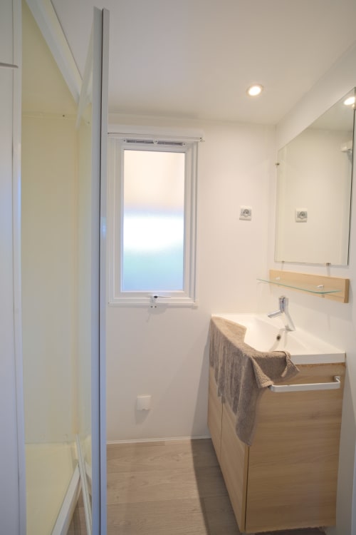 Salle de bain moderne avec meuble vasque en bois, miroir, fenêtre vue mer et douche chez Annick Mobilhome à Vias Plage