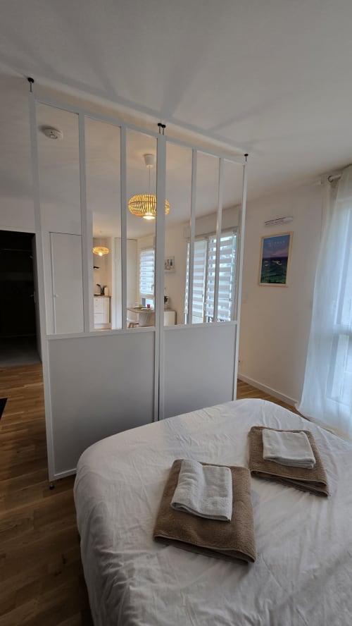 Modern bedroom with glass partition wall in Ô KASTEL apartment at La Fôret-Fouesnant, featuring bed with towels and en-suite