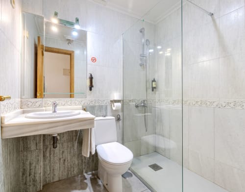 Baño moderno con ducha de cristal, lavamanos blanco y inodoro en el Hostal El Molino de Collado Villalba
