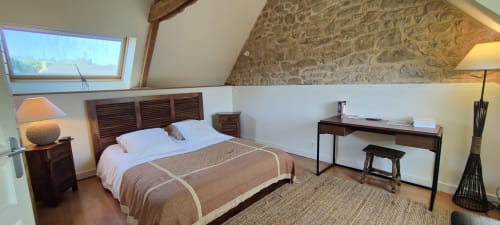 Chambre à l'étage de la villa Mer et Maisons à La Trinité-sur-Mer avec lit en bois, bureau, murs en pierre et vue sur le jardin