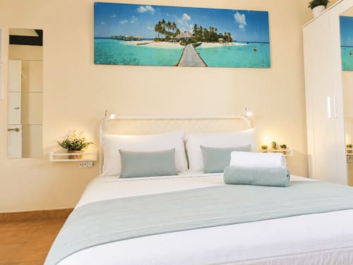 Chambre lumineuse avec lit blanc, oreillers turquoise et décoration tropicale à l'hôtel Sara & Gino à Fuerteventura