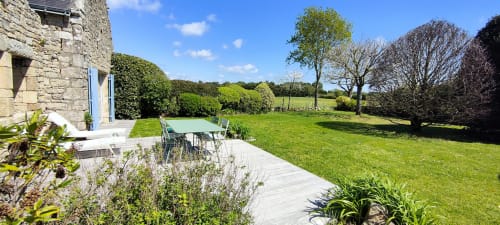 Terrasse-jardin en pierre avec table de repas offrant une vue sur la pelouse paysagée de Mer et Maisons, La Trinité sur Mer