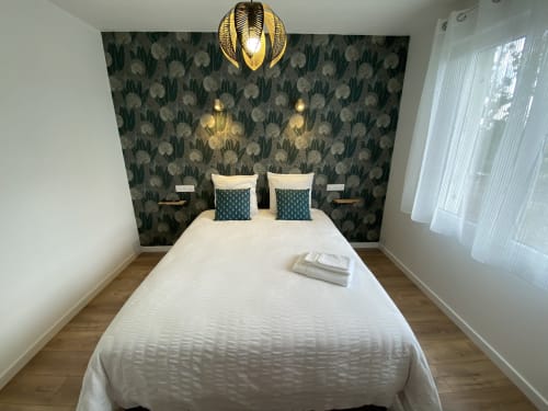 Chambre moderne à La Maison Blanche, Bouguenais avec lit queen-size, papier peint fleuri, luminaire doré et vue sur le jardin.