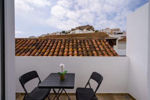 Terraza privada con vistas a la Alcazaba de Salobreña, mesas y sillas negras, flores en maceta, tejado tradicional de barro