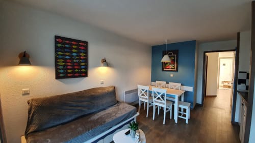 Modern apartment living area with sofa, dining table, blue accent wall, and sea views at Ô CAP COZ, La Fôret-Fouesnant