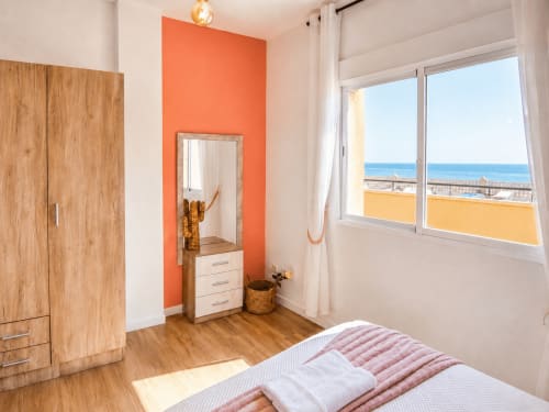 Bright bedroom with sea view at Apartamentos El Calón Playa, featuring wooden wardrobe, orange accent wall, and coastal