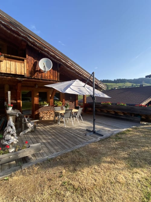 Terrasse avec vue sur les montagnes à La Ferme des Georgières, deck en bois, mobilier de jardin et parasol blanc