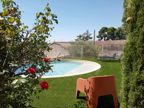 Vue ensoleillée du jardin du gîte Chez Laure & Marc à Plaissan : piscine courbe, pelouse verdoyante, roses rouges et aménagements soignés