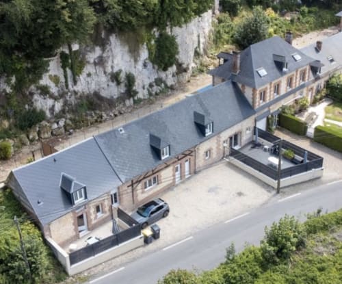 Aerial view of Les Gites De Flaubert villa in Le Héron with slate roof, stone facade, and garden surrounded by cliffs