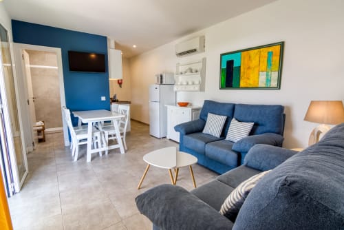 Apartamento estudio moderno en Las Golondrinas con pared azul, sala de estar, cocineta y obras de arte coloridas