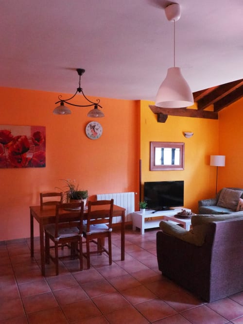 Luminoso salón diáfano con paredes naranjas, mesa de comedor, televisor y cómoda zona de estar en apartamento rural español