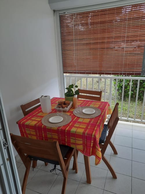 Salle à manger de l'appartement Kay Betty aux Trois-Îlets avec nappe à carreaux rouges, couverts et vue sur le jardin