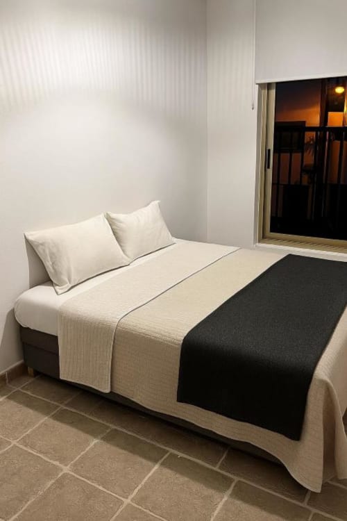 Dormitorio moderno con ropa de cama crema y negra, almohadas blancas y vistas al océano en El HierroStay Apartments en La Restinga.