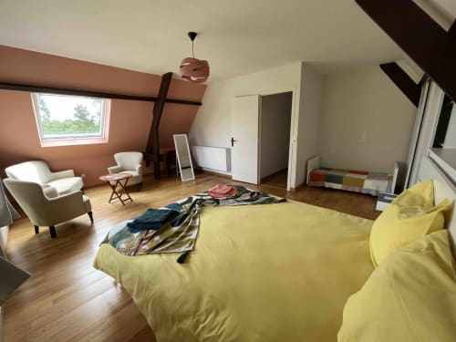 Chambre spacieuse avec literie jaune, fauteuils crème, poutres apparentes et puits de lumière au Domaine du Verger en Auge