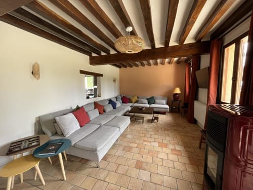 Spacieux séjour de cottage au Domaine du Verger en Auge avec poutres apparentes, canapé gris et carrelage terre cuite