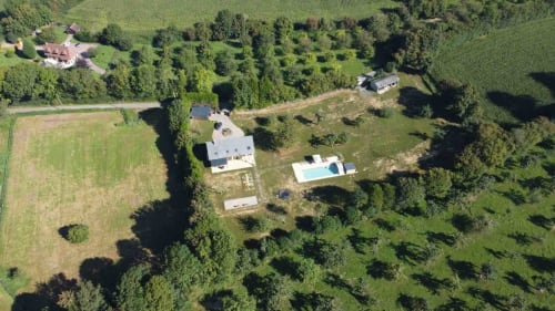 Vue aérienne du gîte Le Domaine du Verger en Auge avec piscine, entouré de verdoyants champs et arbres en Normandie