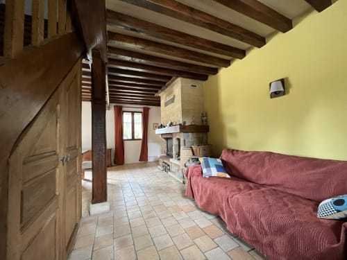 Salon lumineux aux murs jaune vif, poutres en bois apparentes, canapé rouge, cheminée et carrelage en terre cuite au Domaine du