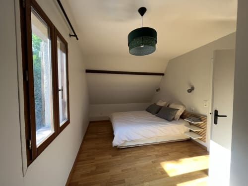 Chambre lumineuse avec parquet, lit queen-size orné de coussins, luminaire suspendu et portes-fenêtres donnant sur le jardin du Domaine