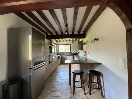 Cuisine moderne avec poutres apparentes, électroménagers inox et coin bar dans le gîte du Domaine du Verger en Auge