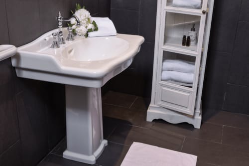 Élégant lavabo sur colonne blanc avec robinetterie chromée et armoire de rangement blanche dans la salle de bains de la Chambre Zenaïde au Petit Manoir de