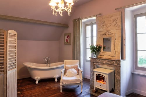 Salle de bain luxueuse au Petit Manoir de Kériolet avec baignoire îlot, cheminée et vue sur le jardin