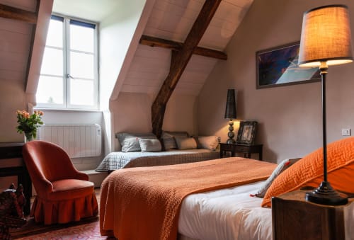 Chambre cosy sous les toits du Petit Manoir de Kériolet à Concarneau avec lits jumeaux, parure orange, poutres en bois et vue sur le jardin