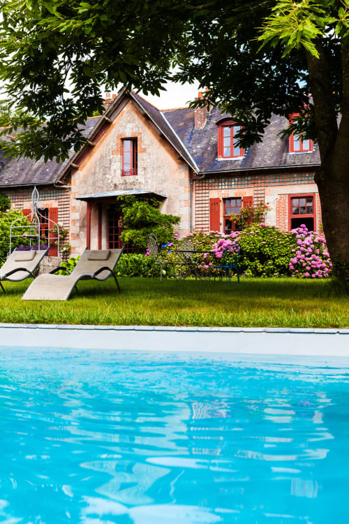 Le Petit Manoir de Kériolet, bord de piscine avec maison en briques, hortensias roses et transats à Concarneau