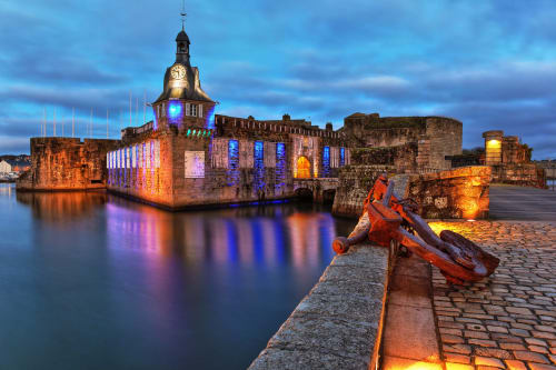 Forteresse historique en pierre illuminée au crépuscule à Concarneau, France avec amarrage et remparts du château reflétés