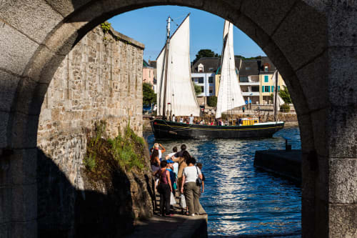 Voûte en pierre encadrant un voilier et des touristes au port de Concarneau, France près du Petit Manoir de Kériolet