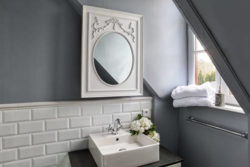 Salle de bain élégante au Petit Manoir de Kériolet avec carrelage métro blanc, miroir ovale orné et serviettes blanches fraîches près de la fenêtre